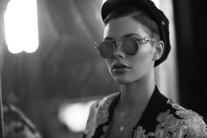 Monochrome portrait of a woman wearing round sunglasses and a dark cap by photographer Frankie Batista.