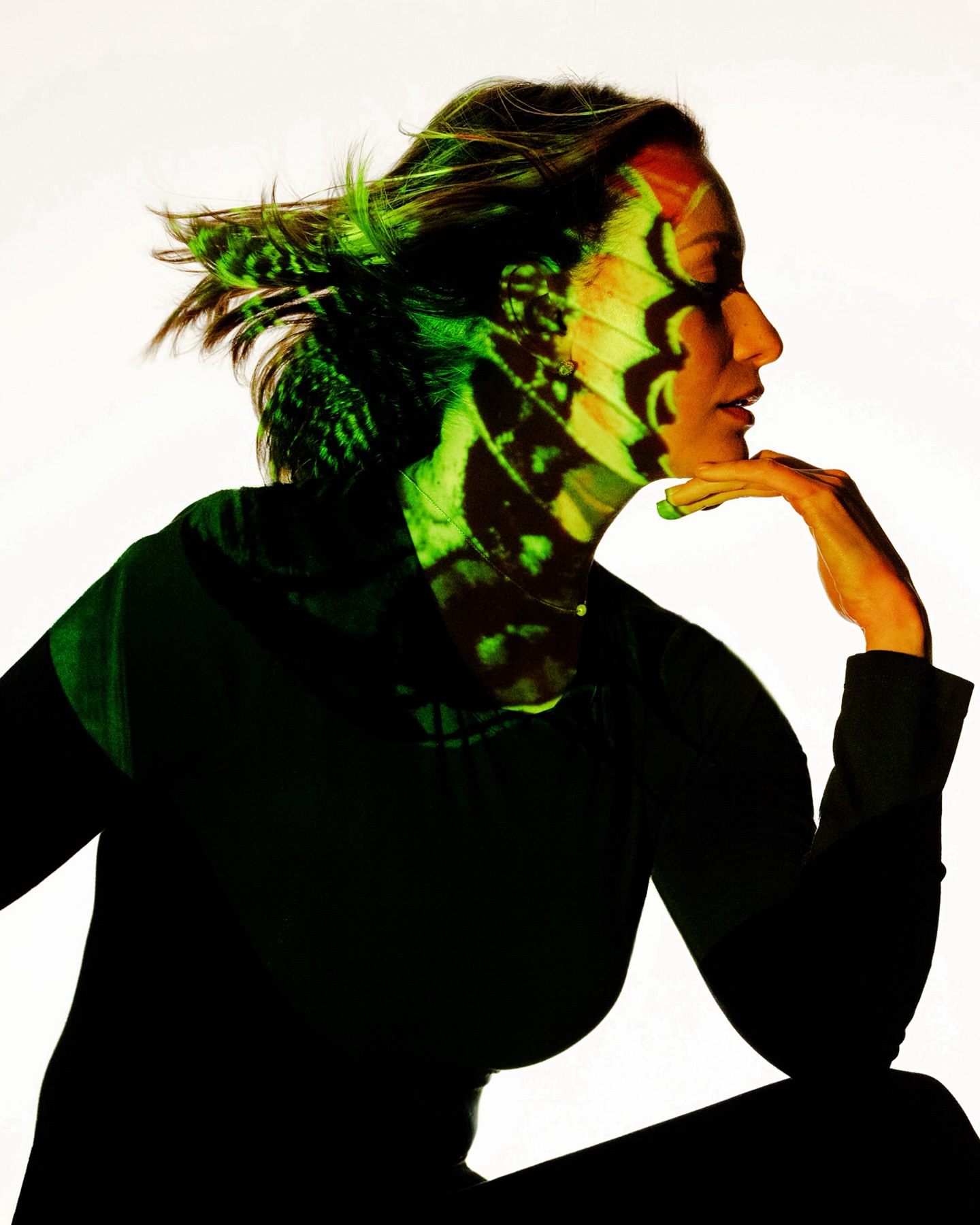 Woman in profile with butterfly wing pattern on her face and upper body in a studio with a light background.
