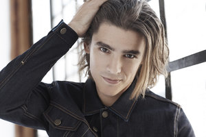 Close-up portrait of a man with long hair wearing a dark denim jacket running his hand through his hair.