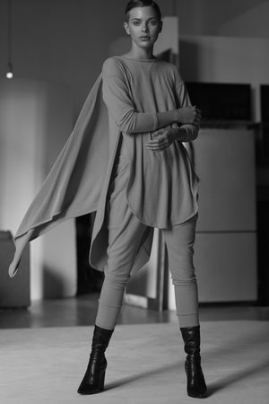 Elegant woman in draped tunic and leggings poses in black ankle boots indoors in a black and white fashion shot.  Modern fashion.