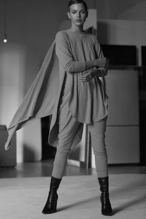 Elegant woman in draped tunic and leggings poses in black ankle boots indoors in a black and white fashion shot.  Modern fashion.