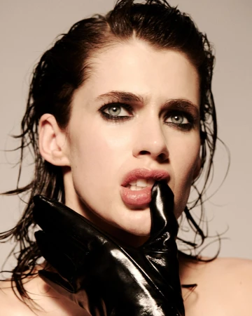 Close-up portrait of a woman with wet dark hair and a black glove touching her lips, featuring dramatic makeup and a neutral background.