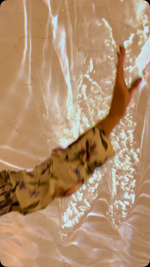Person in floral long-sleeved shirt extending arm against a textured background with light reflections, creating a surreal, artistic effect.