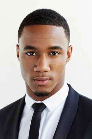 Portrait of a black man with short dark hair wearing a white collared shirt, black tie, and dark suit jacket.
