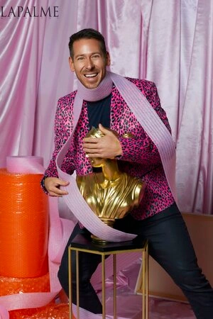 Man wearing a pink leopard print blazer and pale lavender scarf holding a gold bust sculpture by photographer Frankie Batista