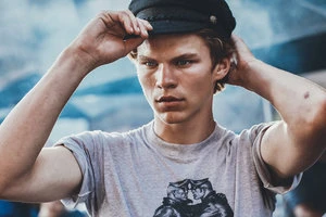 Young man in a graphic t-shirt adjusting a dark cap outdoors by Frankie Batista