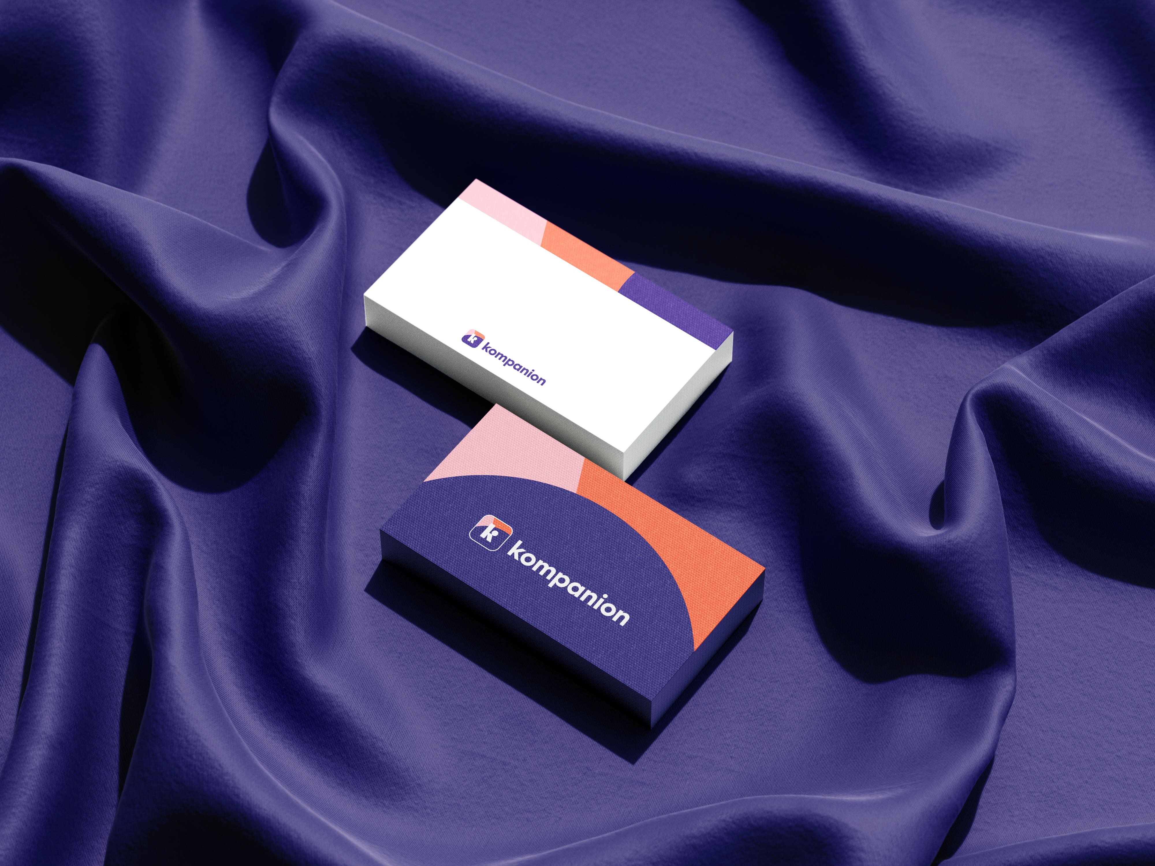Two business cards are placed on a crumpled indigo textile, with the cards displaying the company name 'Kompanion' and color-blocked accents.