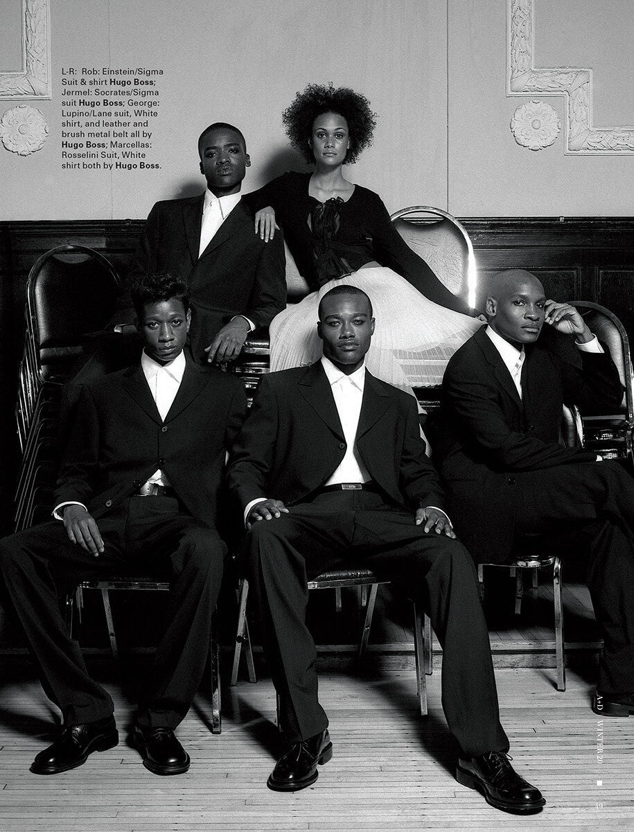Monochrome fashion shoot featuring a group of four men and a woman wearing formal black suits and dress sitting on chairs.
