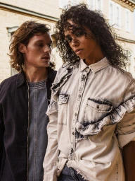 Two models outdoors, a woman in a light acid-wash denim shirt and a man in a dark jacket by David Leslie Anthony.