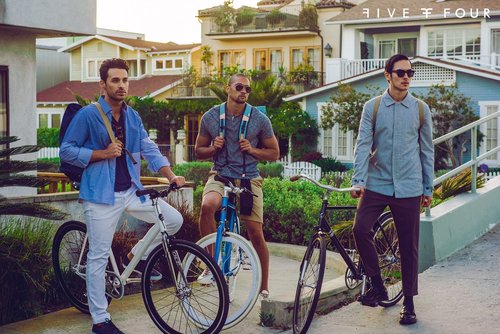 Three stylish men pose with bikes in a residential neighborhood; the shot captures urban lifestyle and casual fashion.