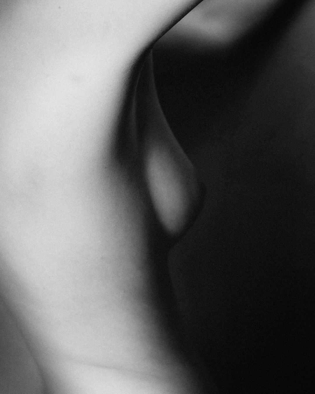 Monochrome nude portrait of adult female with focus on smooth skin and soft shadows, creating a sensual, artistic photograph.