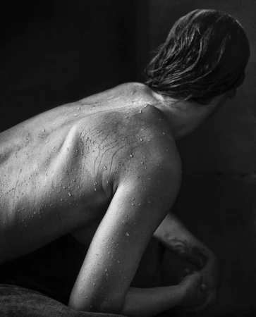 Close-up monochrome portrait of a person with wet skin and water droplets glistening across their back and shoulder by Omar Cruz