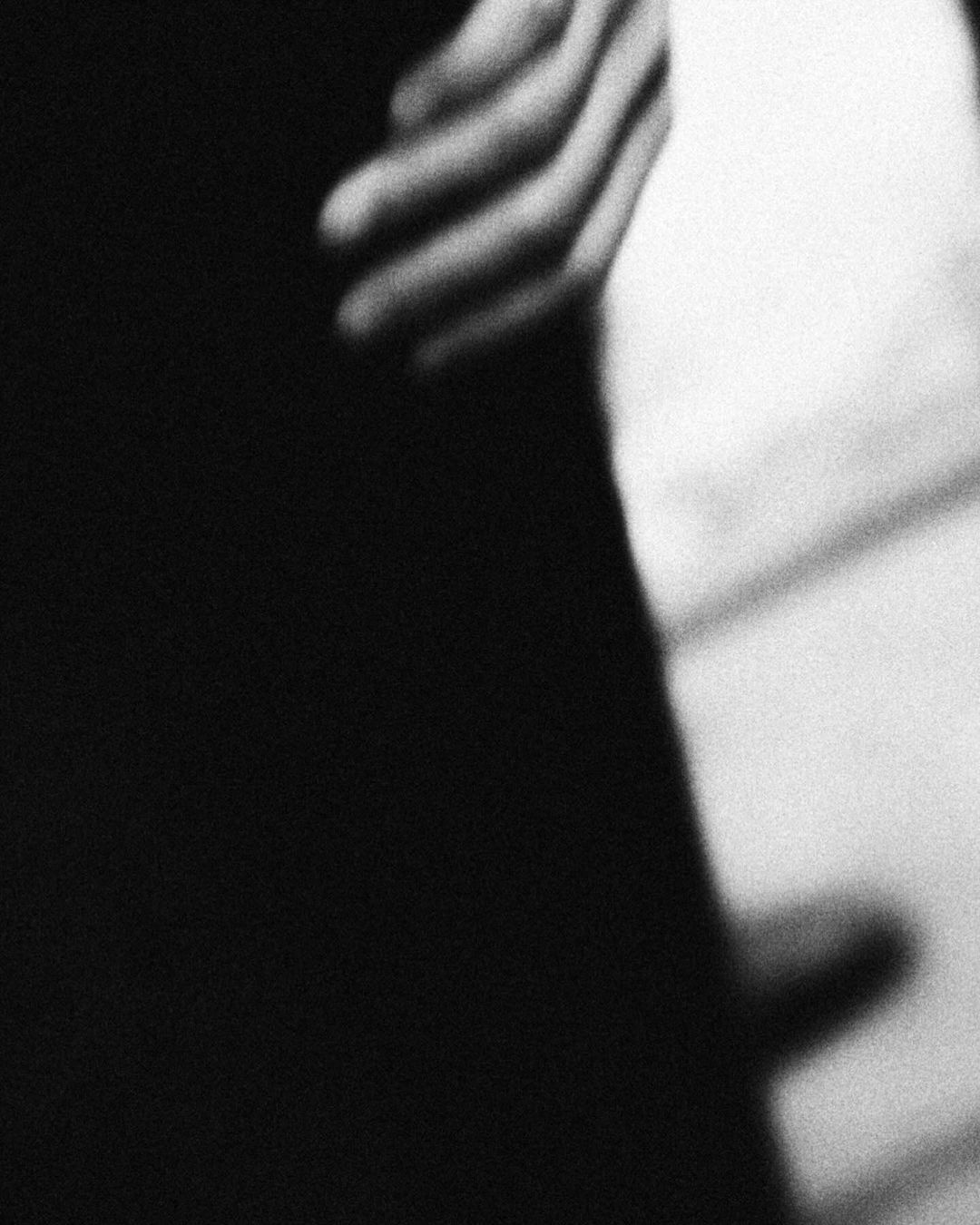 Close-up of a person's hand resting against a dark garment with heavy black-and-white film grain
