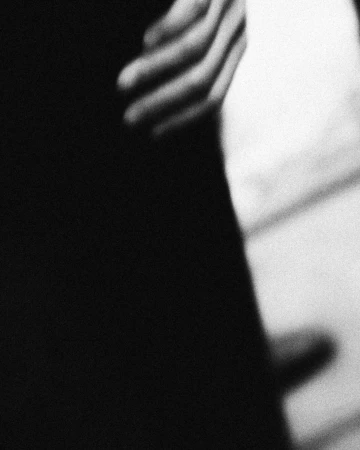 Close-up of a person's hand resting against a dark garment with heavy black-and-white film grain
