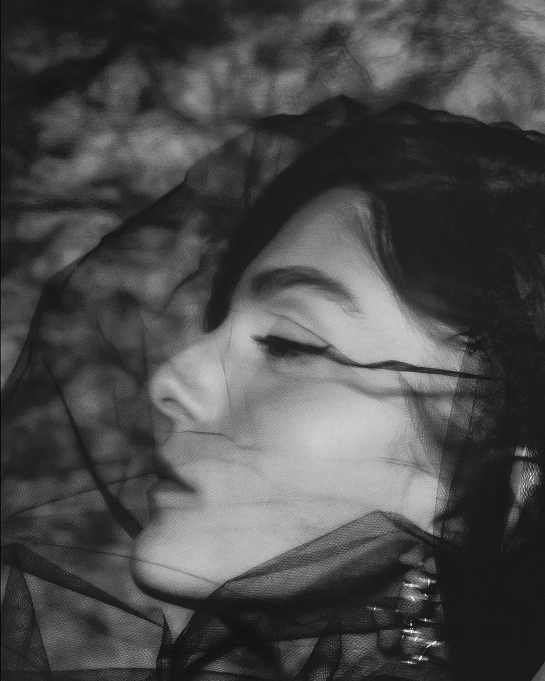 Black and white portrait of a woman in a veil. The image focuses on her facial features and the texture of the veil.