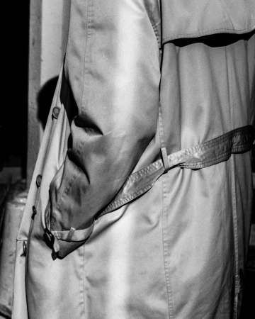 Monochrome close-up of a person wearing a belted trench coat with hands in pockets photographed by Omar Cruz