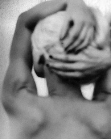 Monochrome portrait of a person's head and shoulders with hands held behind their head, creating a sense of intimacy.