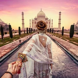 Woman in traditional Indian dress is being led toward the Taj Mahal by a hand in a romantic pose with a beautiful sky.