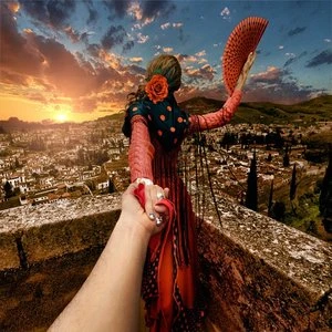 Follow-me shot of a woman in traditional Spanish dress holding a fan on a rooftop with an expansive city and sunset view.