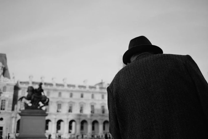 Man wearing a fedora hat and textured jacket viewed from behind with an old building in the background