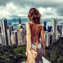 Woman in backless grey dress holding hands with photographer overlooking city skyline from a high vantage point