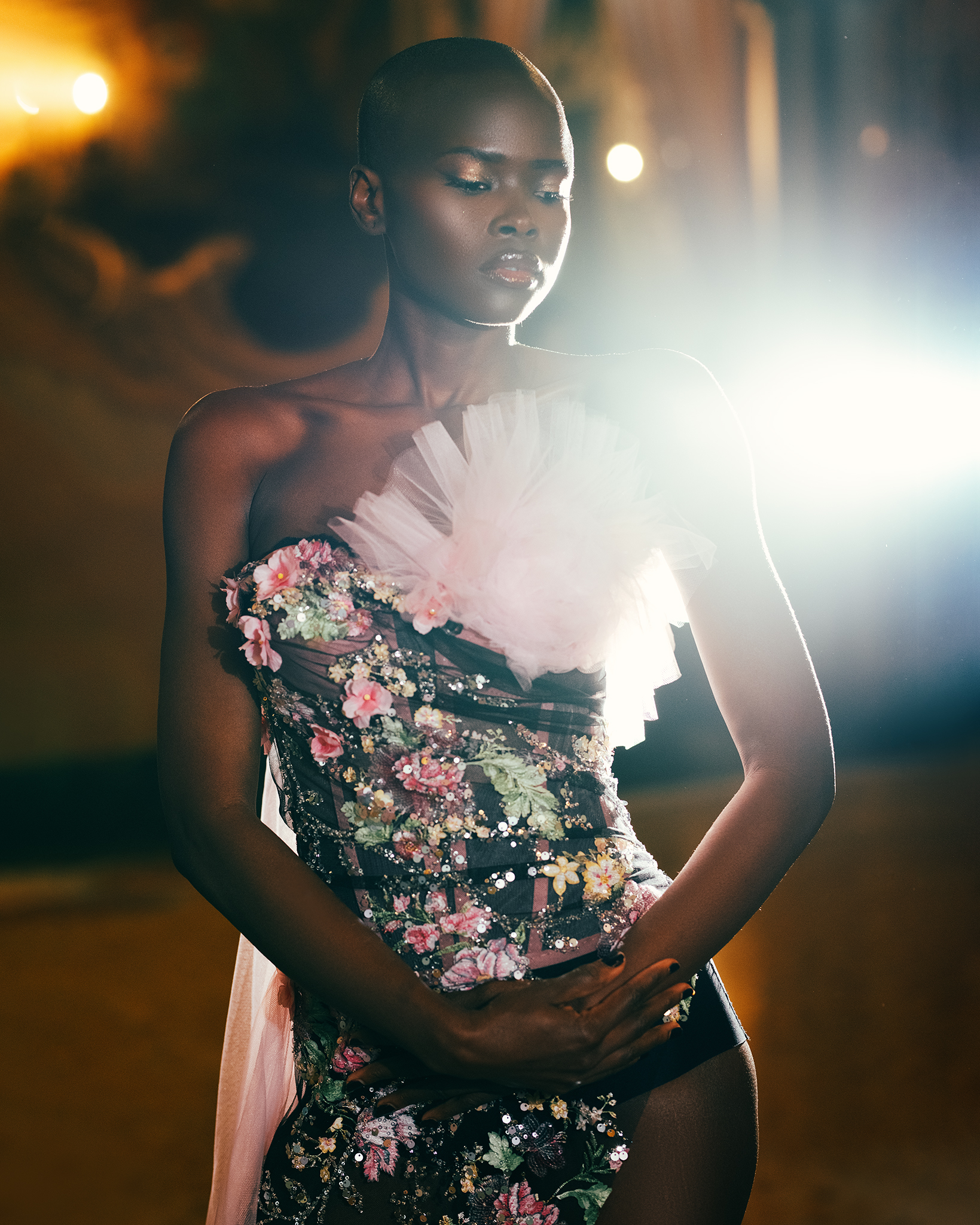 Elegant woman in floral dress with pink tulle posing under bright lights, fashion-forward, beauty and elegance in studio setting.