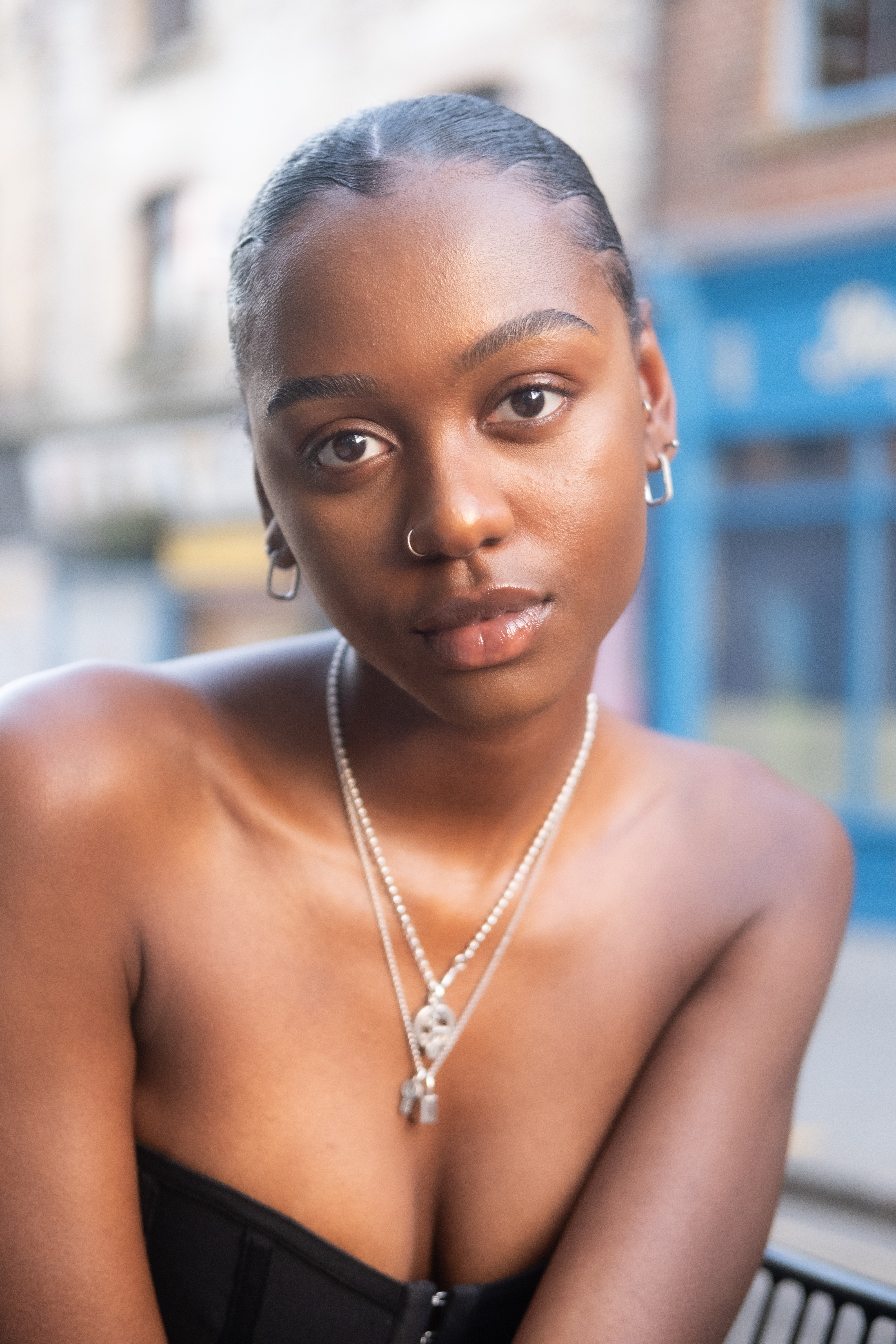 Close-up portrait of a young African-American woman with an elegant hairstyle wearing jewelry, set against a blurred outdoor background.