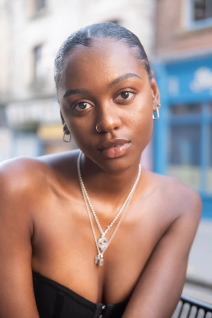 Close-up portrait of a young African-American woman with an elegant hairstyle wearing jewelry, set against a blurred outdoor background.