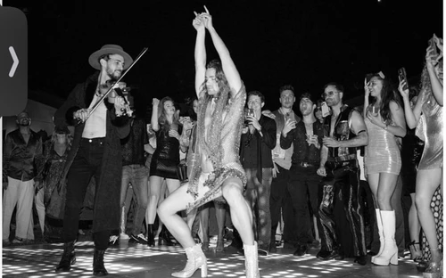 Monochrome image of musician Maury Hechavarria dancing in a metallic outfit surrounded by a crowd at an event in Los Angeles.