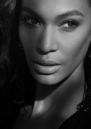 Black and white portrait of a woman with medium skin tone, wearing dark clothing, posing with a neutral expression, and decorative earrings.
