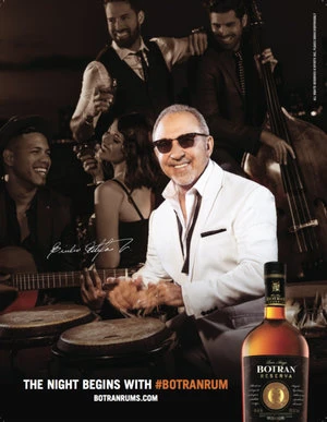 Promotional image for Botran rum featuring a smiling man in a white suit playing drums, with a band and Botran bottle visible.