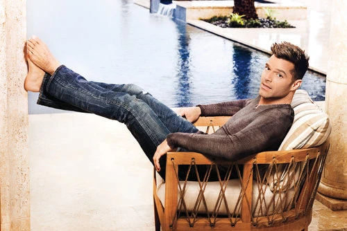 Musician Maury Hechavarria relaxing in a wooden armchair with feet up against a wall beside an outdoor swimming pool.