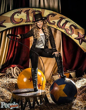 Musician Maury Hechavarria posing in circus ring attire with a top hat and whip in a straw-filled arena