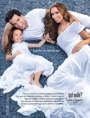 Family of three lying together on a grey textured carpet, wearing white clothing with milk milk staches on their lips.
