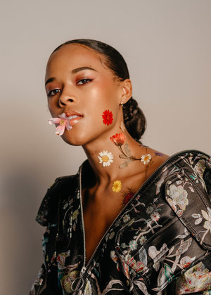 Portrait of a woman with flowers on her face and chest wearing a floral print jacket against a neutral background. Beauty concept.