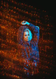 Woman in a textured sparkly sweater with arms raised amid a field of warm and cool colored bokeh lights