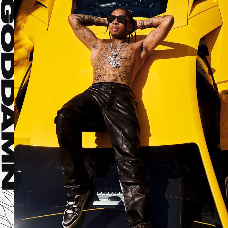 Shirtless man with tattoos and sunglasses reclines on a yellow sports car, wearing black leather pants and black-and-white sneakers.