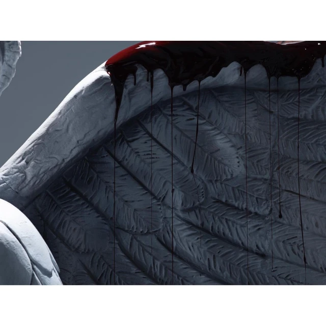 Close-up of a stone angel wing statue with dark liquid dripping down, creating a dark and somber visual.