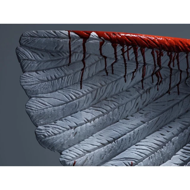 Close-up of a white, feathered angel wing with red liquid dripping down, creating a dramatic and slightly unsettling visual.
