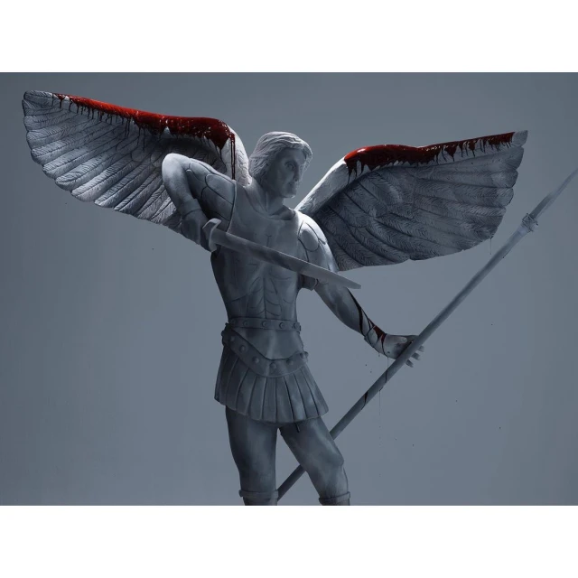 Winged male statue with sword and spear, armor, and simulated blood accents against a light grey background in a studio setting.