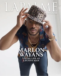 Marlon Wayans wearing a leopard print bucket hat and glasses adjusts his hat against a white background.