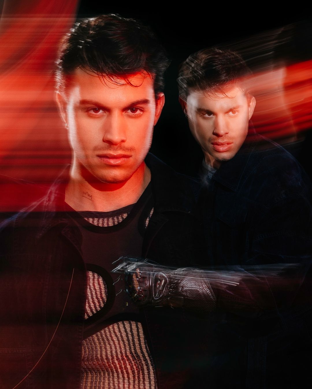 Portrait of a young adult man with a serious expression, featuring a blurred background and red light trails. The composition highlights his features.