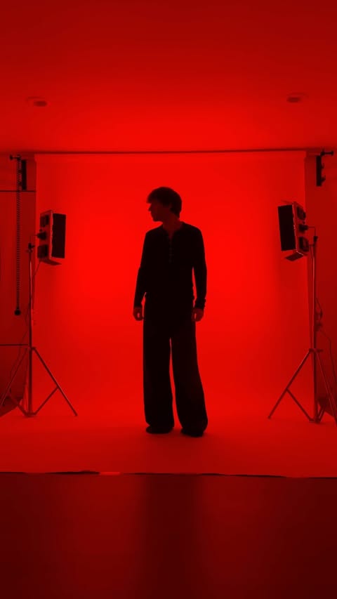 Full body shot of a person in wide leg suit standing in photo studio with red lighting and two light stands in the background.