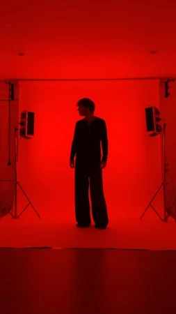 Full body shot of a person in wide leg suit standing in photo studio with red lighting and two light stands in the background.