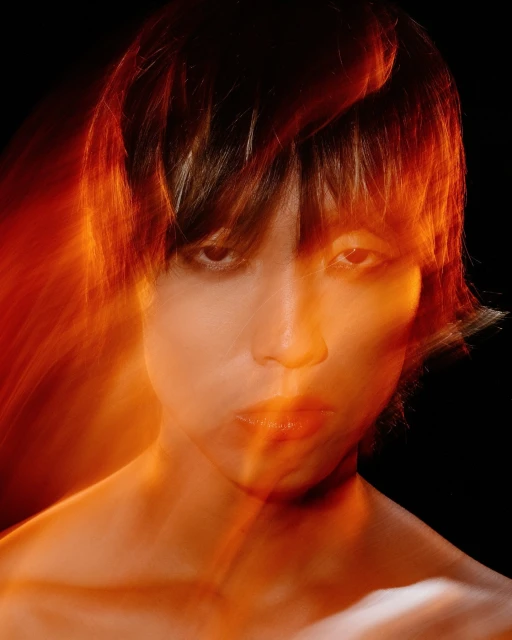 Portrait of a person with brown hair, eyes looking at the camera in a photo studio setting. The warm lighting highlights facial details.