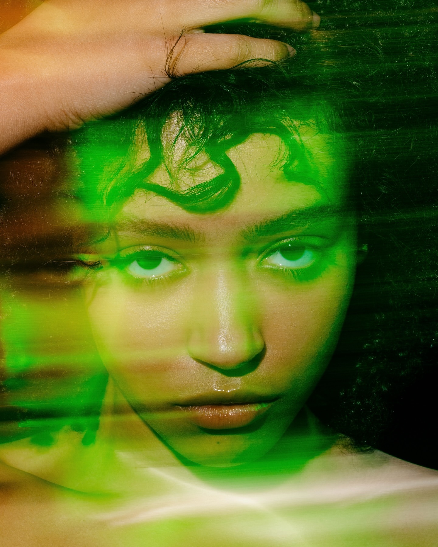 Portrait of a young woman with green lighting, hand on head, and soft focus. The girl is looking directly at the camera.