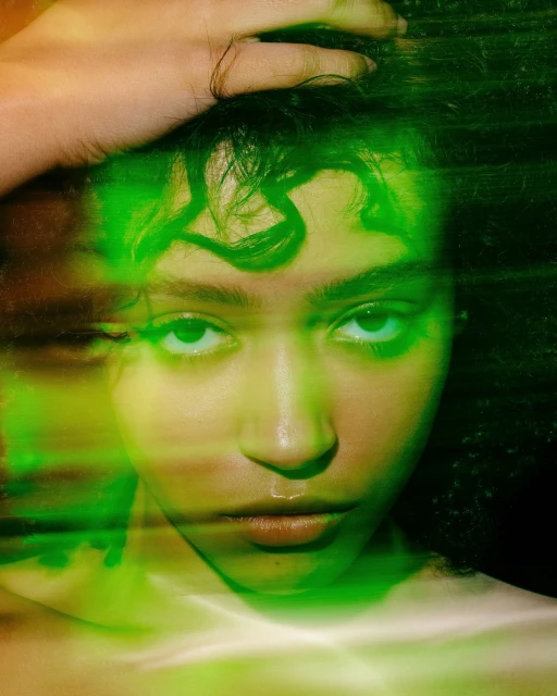 Portrait of a young woman with green lighting, hand on head, and soft focus. The girl is looking directly at the camera.