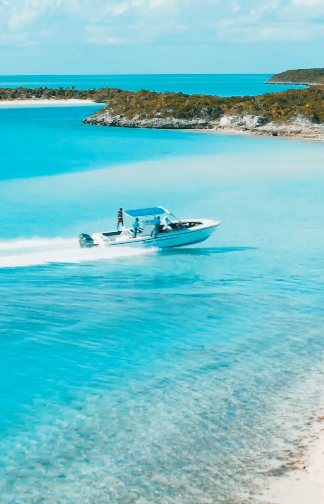 A powerboat carrying several people cruises swiftly through clear, turquoise waters near a tropical island with lush vegetation.
