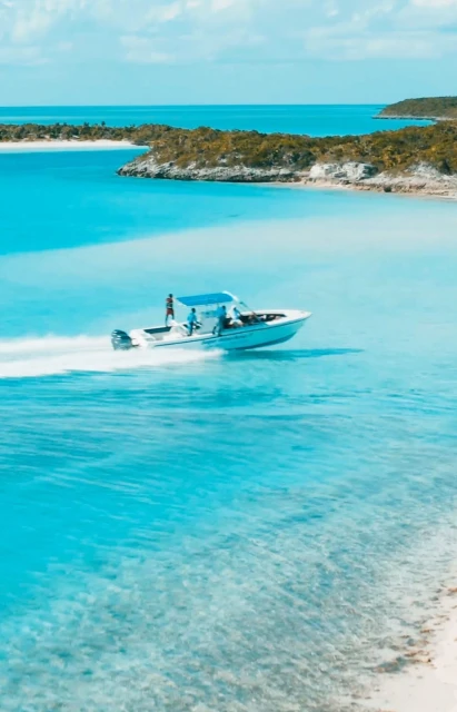 A powerboat carrying several people cruises swiftly through clear, turquoise waters near a tropical island with lush vegetation.