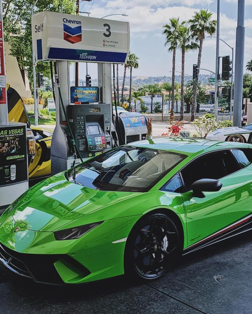 Green Lamborghini parked at a gas station, with palm trees and a hillside in the background, showcasing automotive design and sunny California lifestyle.